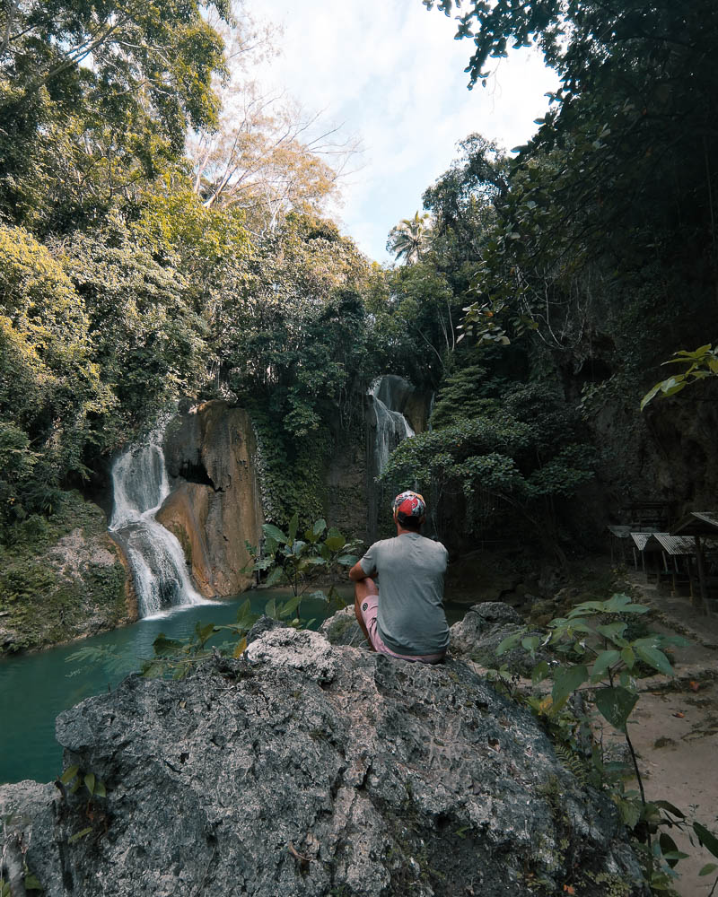A sat in the possible place staring at the cascade surrounded in a natural landscape