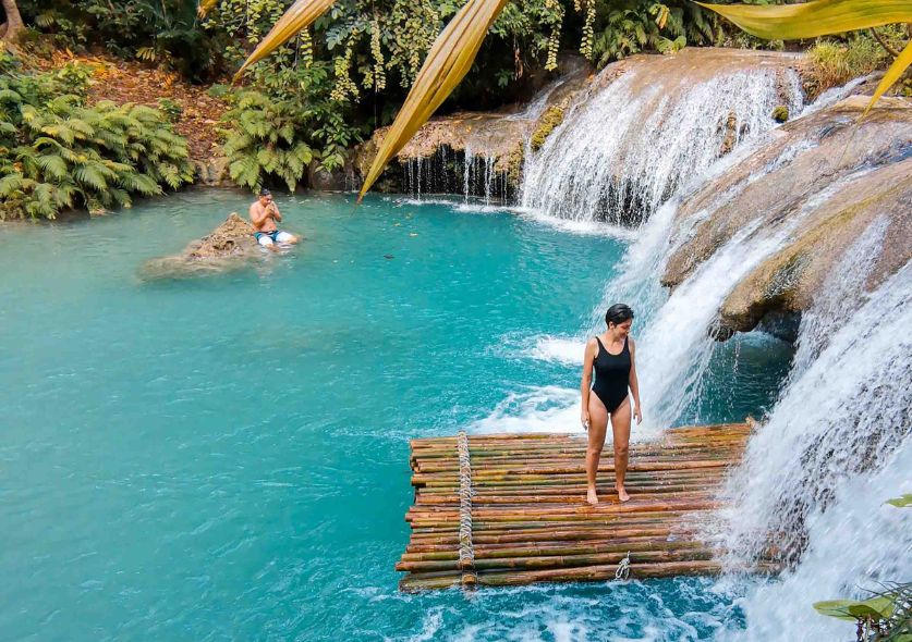 Jacqueline on a bamboo raft in a turquoise pool near a a cascade