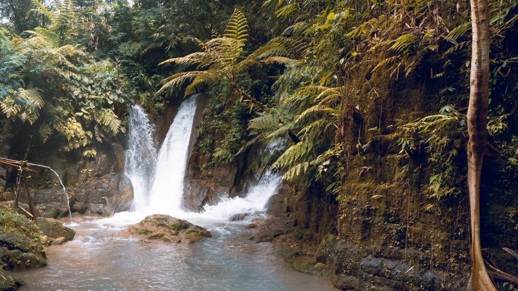 The 3 cascades ar curug cisanca surrounded in jungle and plunging into a shallow pool beneath