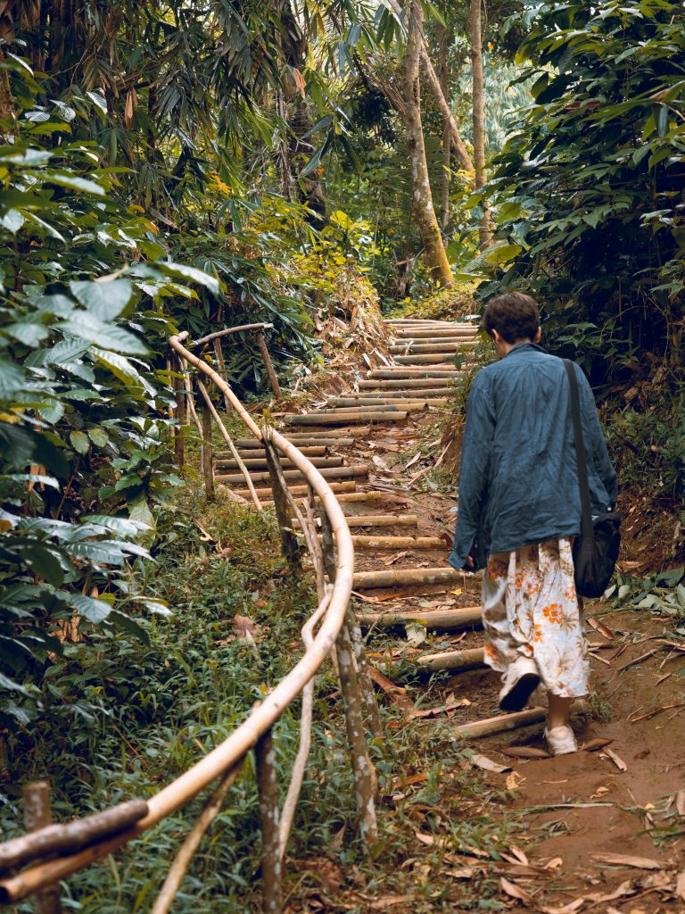 Jacqueline walking up a raw flight of stairs carved out of the soil and bamboo steps and a bamboo railing