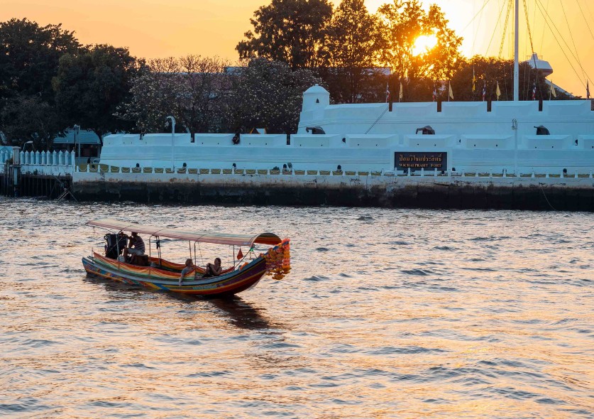 A longtail boat floating in a river as the sun is setting.