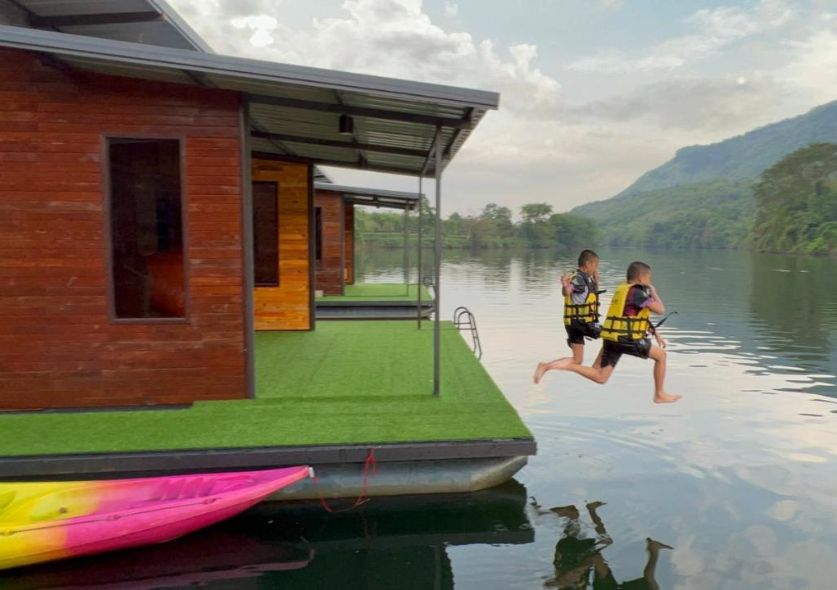 Kids jumping off a floating bungalow in a river surrounded in mountains and jungle