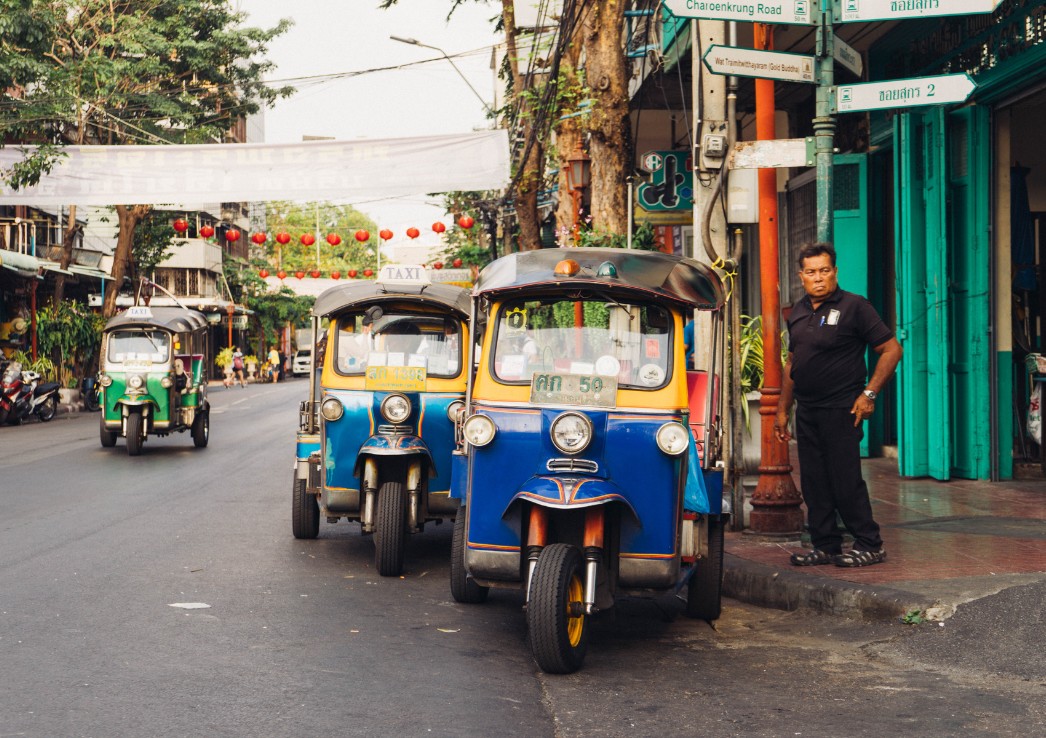 A driver standing next to his tuk tuk